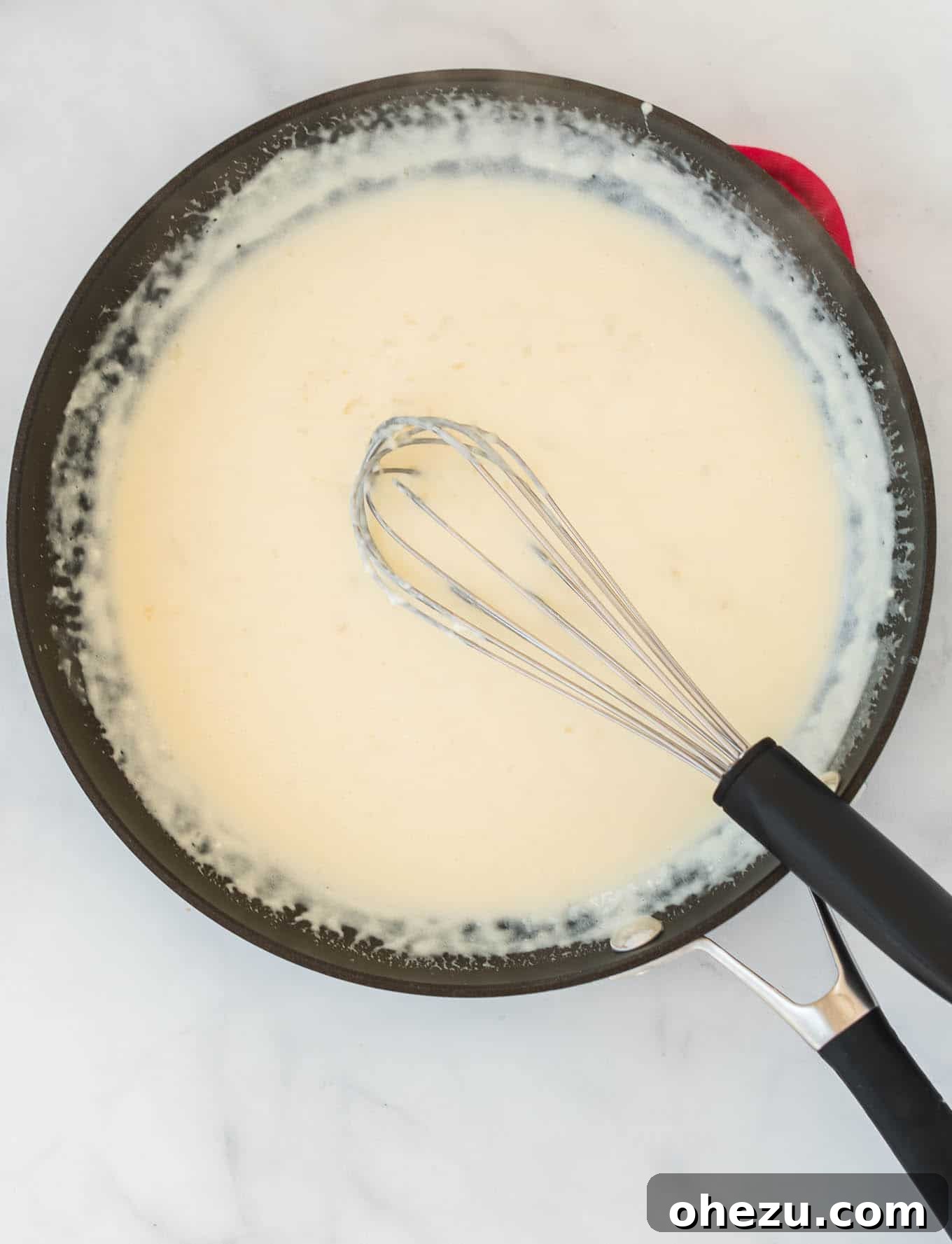 Cream cheese pasta sauce being whisked in a skillet, showing its smooth texture