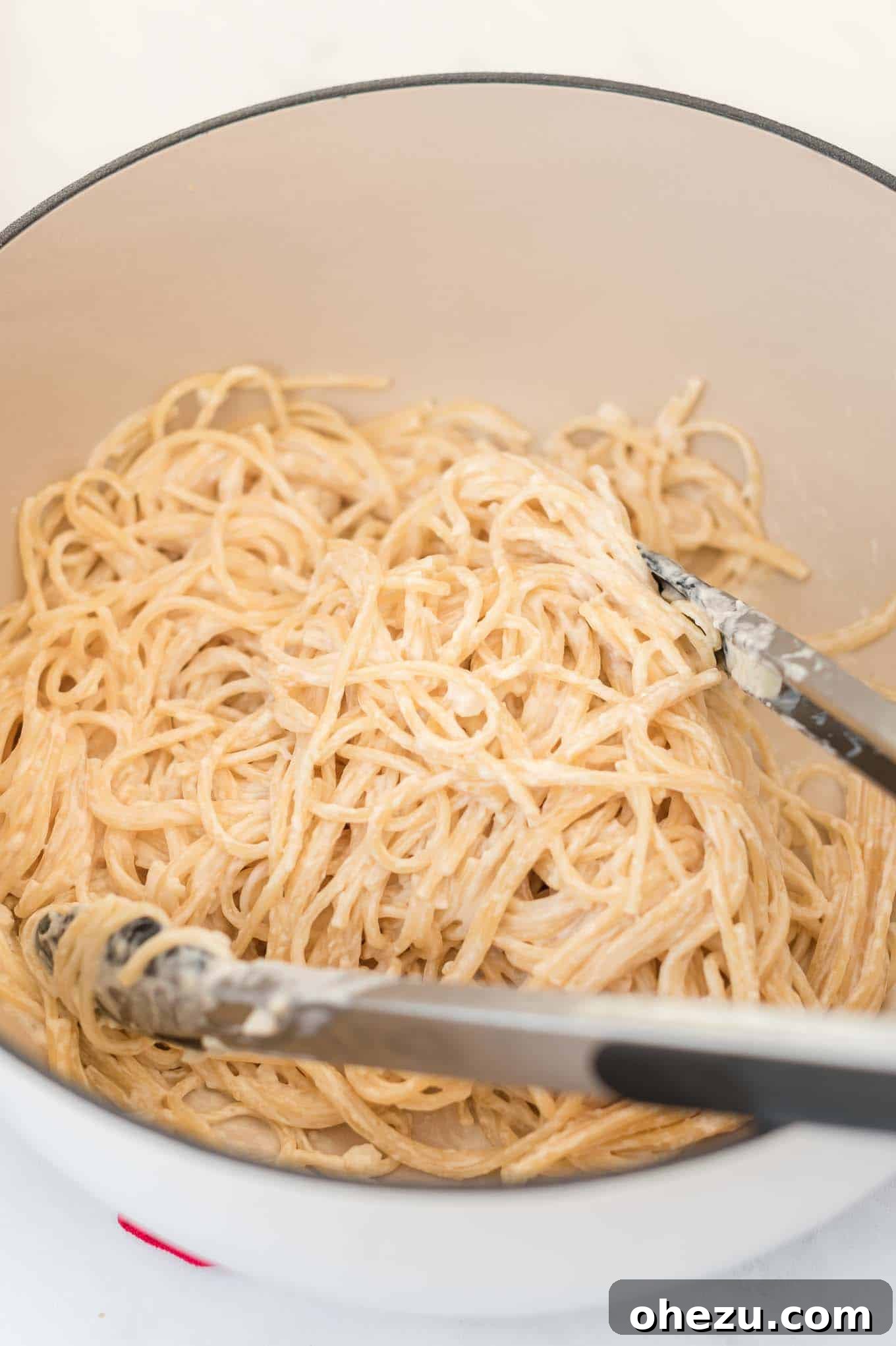Cream cheese pasta served in a white dutch oven with tongs, ready to eat