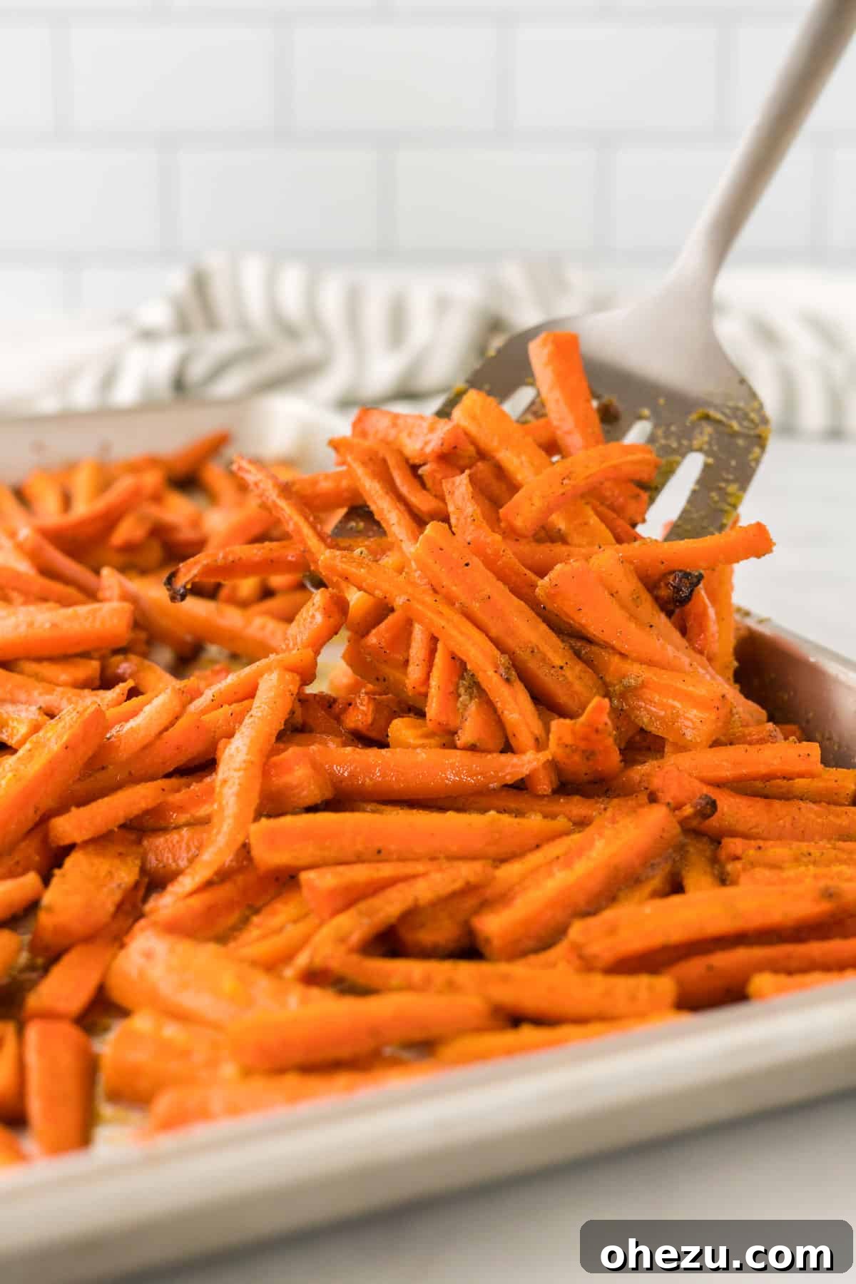 The Ultimate Roasted Carrots 2 Spatula taking a serving of golden brown roasted carrots from a pan, highlighting their caramelized edges and tender texture.