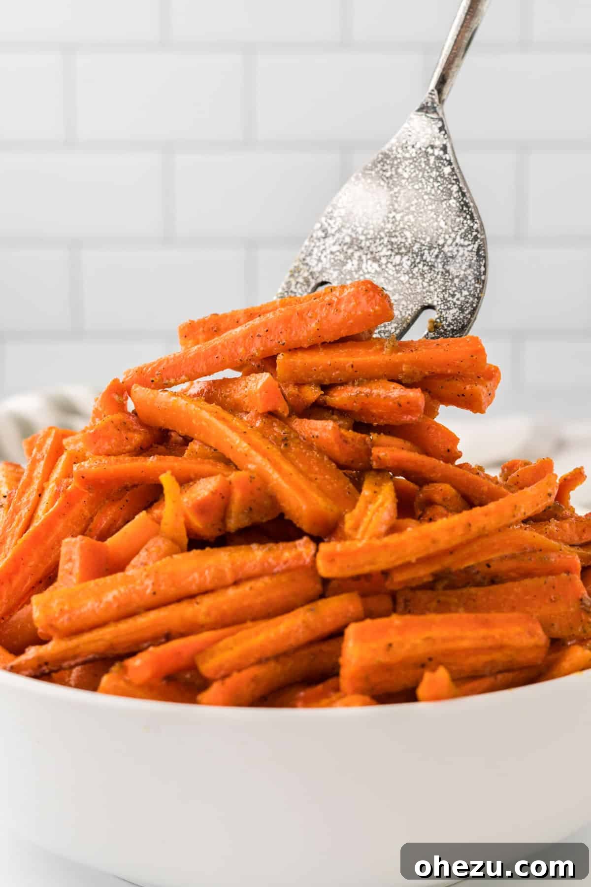 The Ultimate Roasted Carrots 11 A kitchen spatula carefully scooping a serving of tender, caramelized roasted carrots from a pristine white serving bowl, indicating they are ready to be plated and savored.