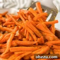 A close-up of a spatula taking a serving of golden brown roasted carrots from a pan.