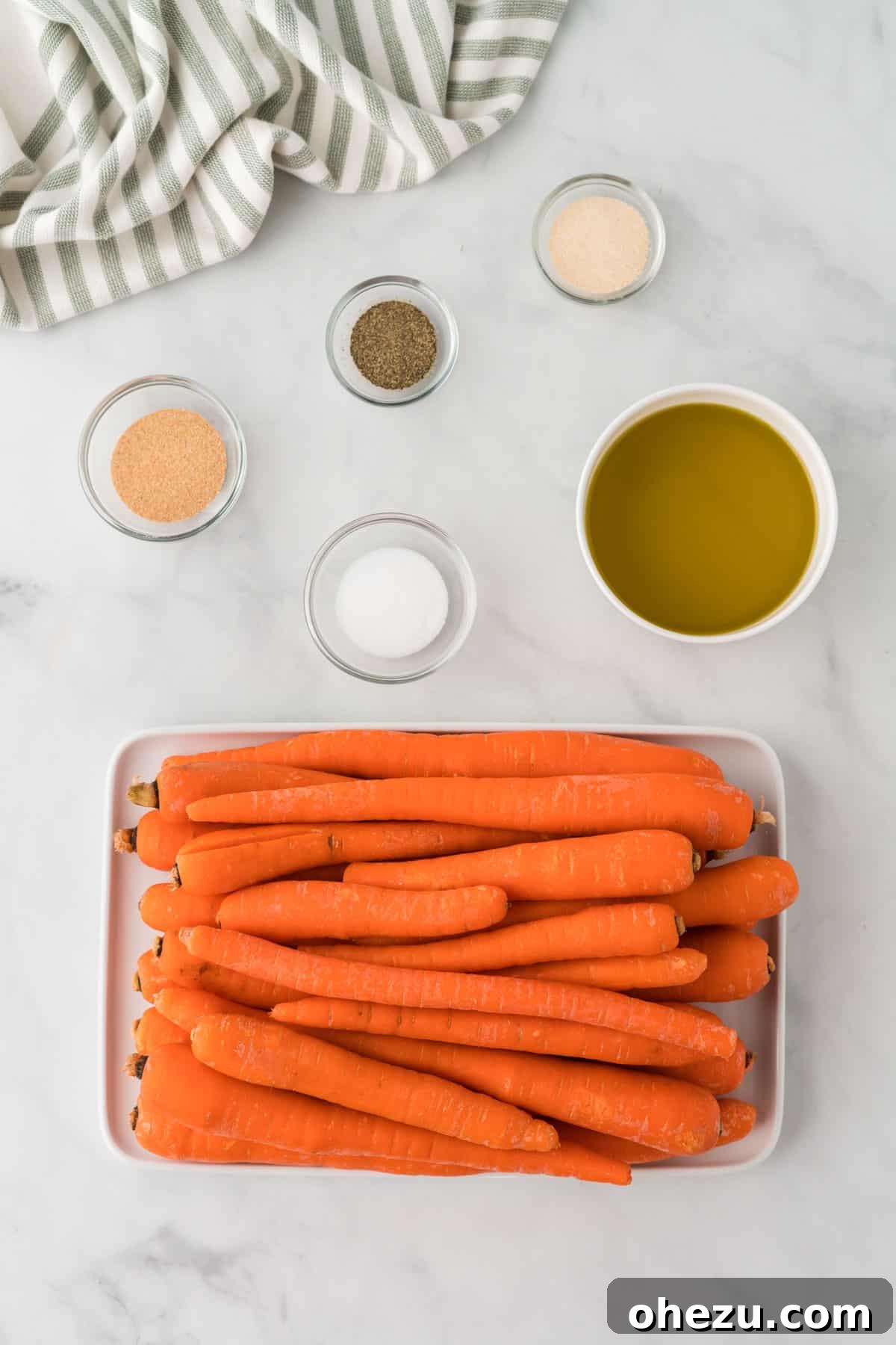 The Ultimate Roasted Carrots 3 A selection of fresh whole carrots, small bowls of garlic powder, onion powder, salt, pepper, and a bottle of olive oil, neatly arranged as ingredients for roasted carrots.