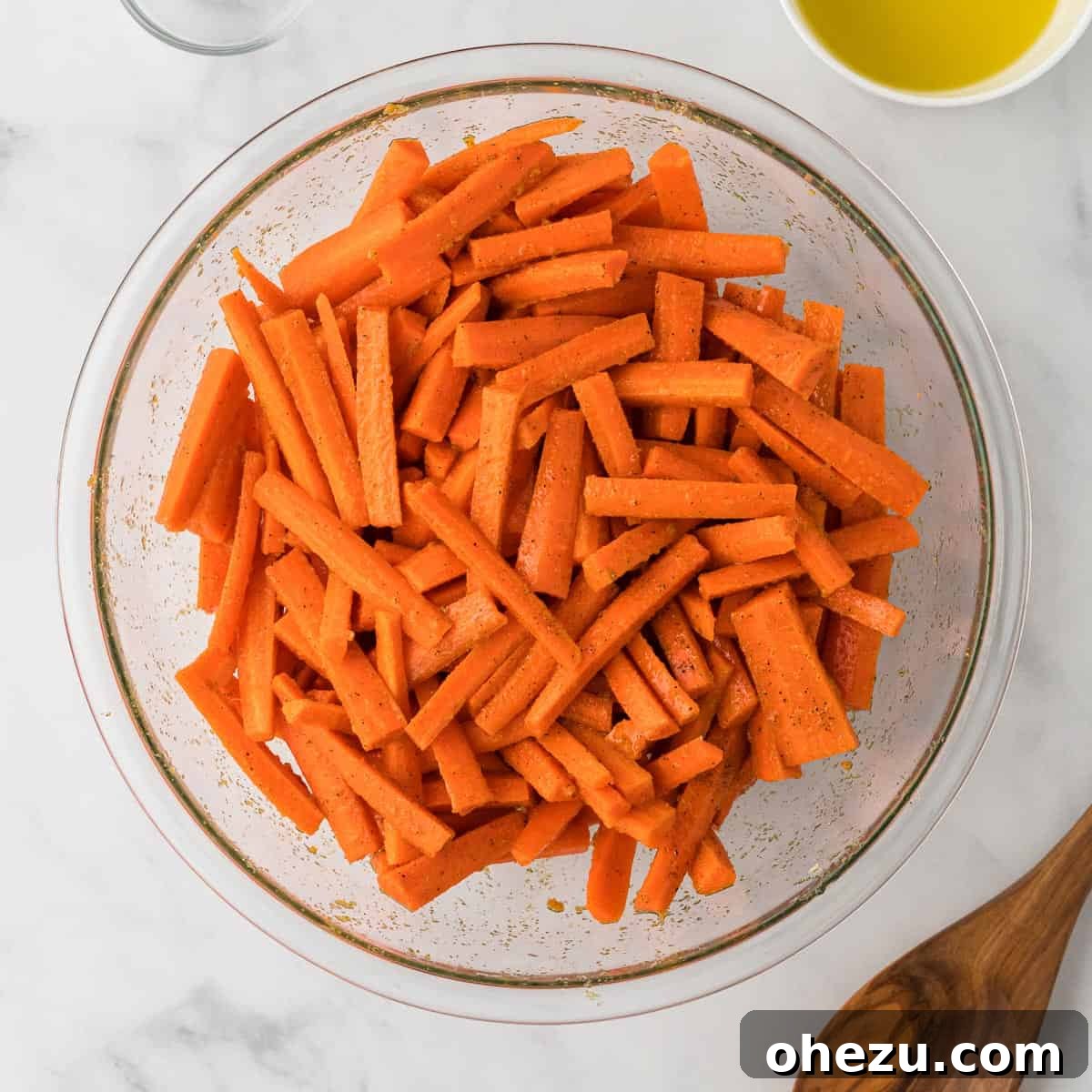 The Ultimate Roasted Carrots 7 Sliced carrots thoroughly mixed and glistening with olive oil and spices in a large bowl, perfectly coated and ready for the roasting process.