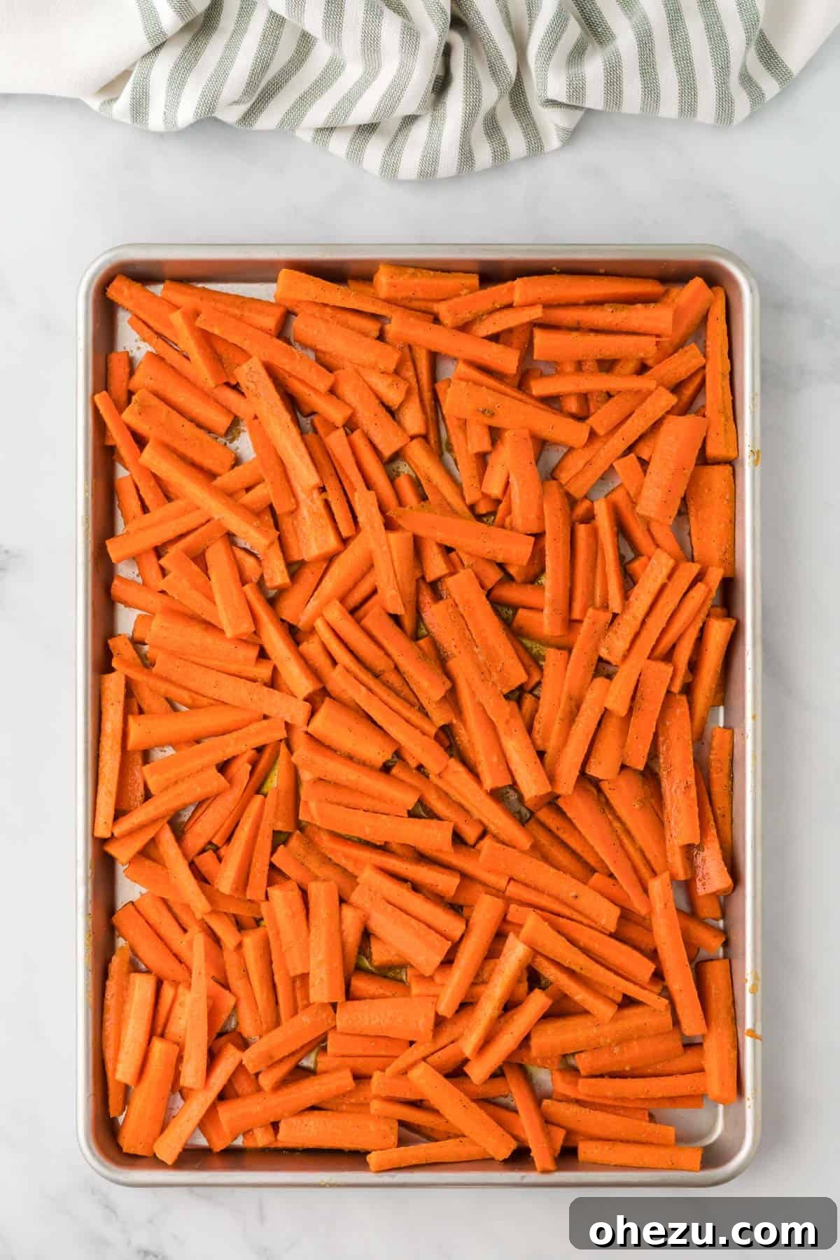 The Ultimate Roasted Carrots 8 Seasoned carrots spread in a perfectly even, single layer on a nonstick baking sheet, meticulously arranged and ready for the intense heat of the oven.