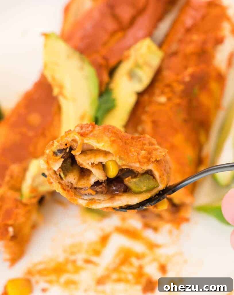 A close-up shot of a fork lifting a bite of a vegan enchilada, showing the rich filling and creamy sauce, emphasizing its delicious texture.