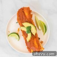 Two vegan enchiladas on a white plate topped with avocado and cilantro, with limes on the side