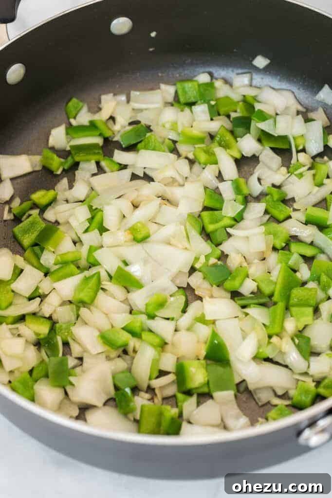 Diced white onion and chopped bell pepper sizzling in olive oil in a hot skillet, ready for the next ingredients to be added for the enchilada filling.