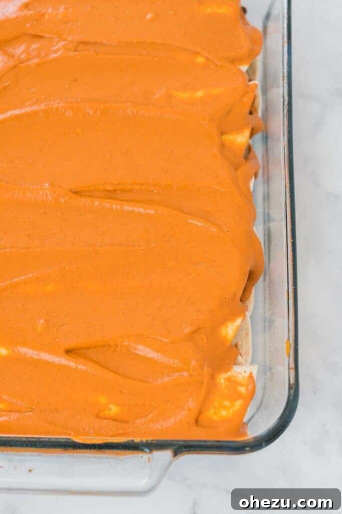 Another view of the perfectly rolled and sauced vegan enchiladas in a baking dish, highlighting their readiness for the oven and the rich topping.