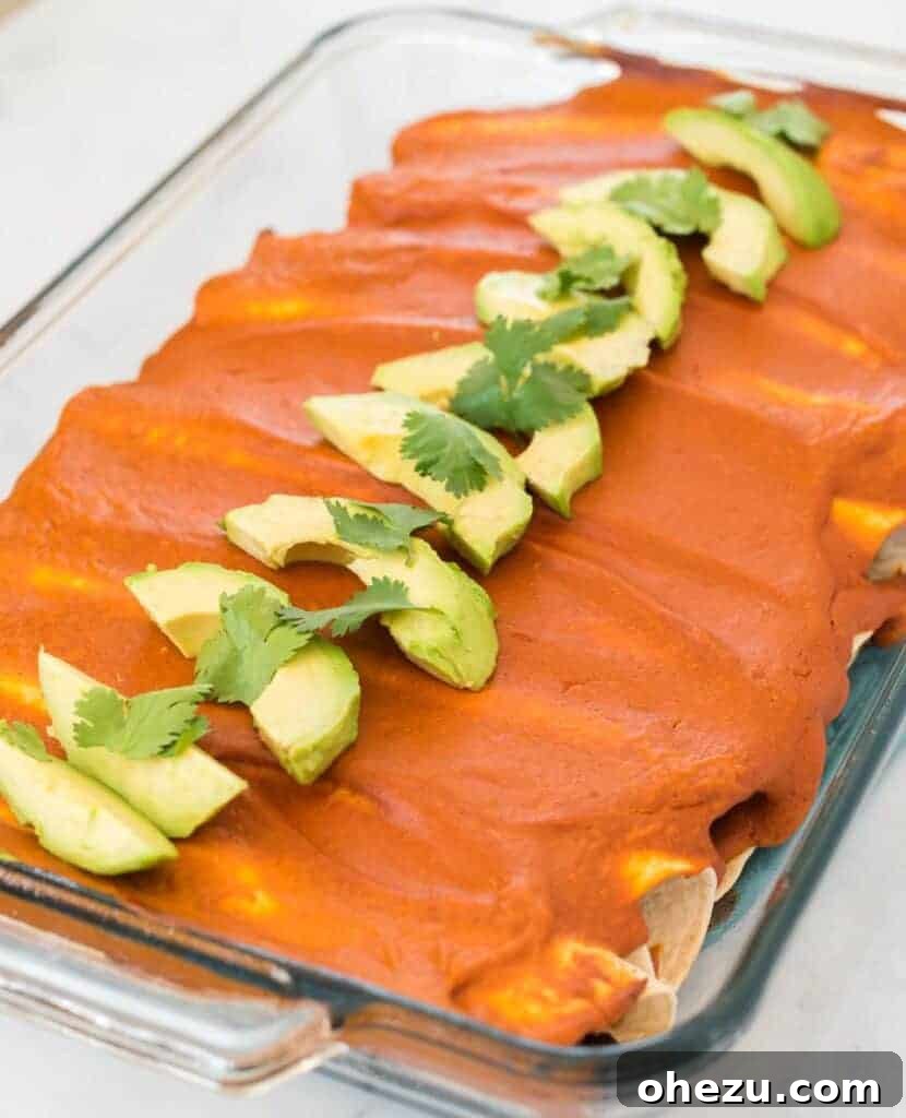 Another enticing shot of freshly baked vegan enchiladas, topped with vibrant avocado and cilantro, alongside fresh lime wedges, ready to be served.