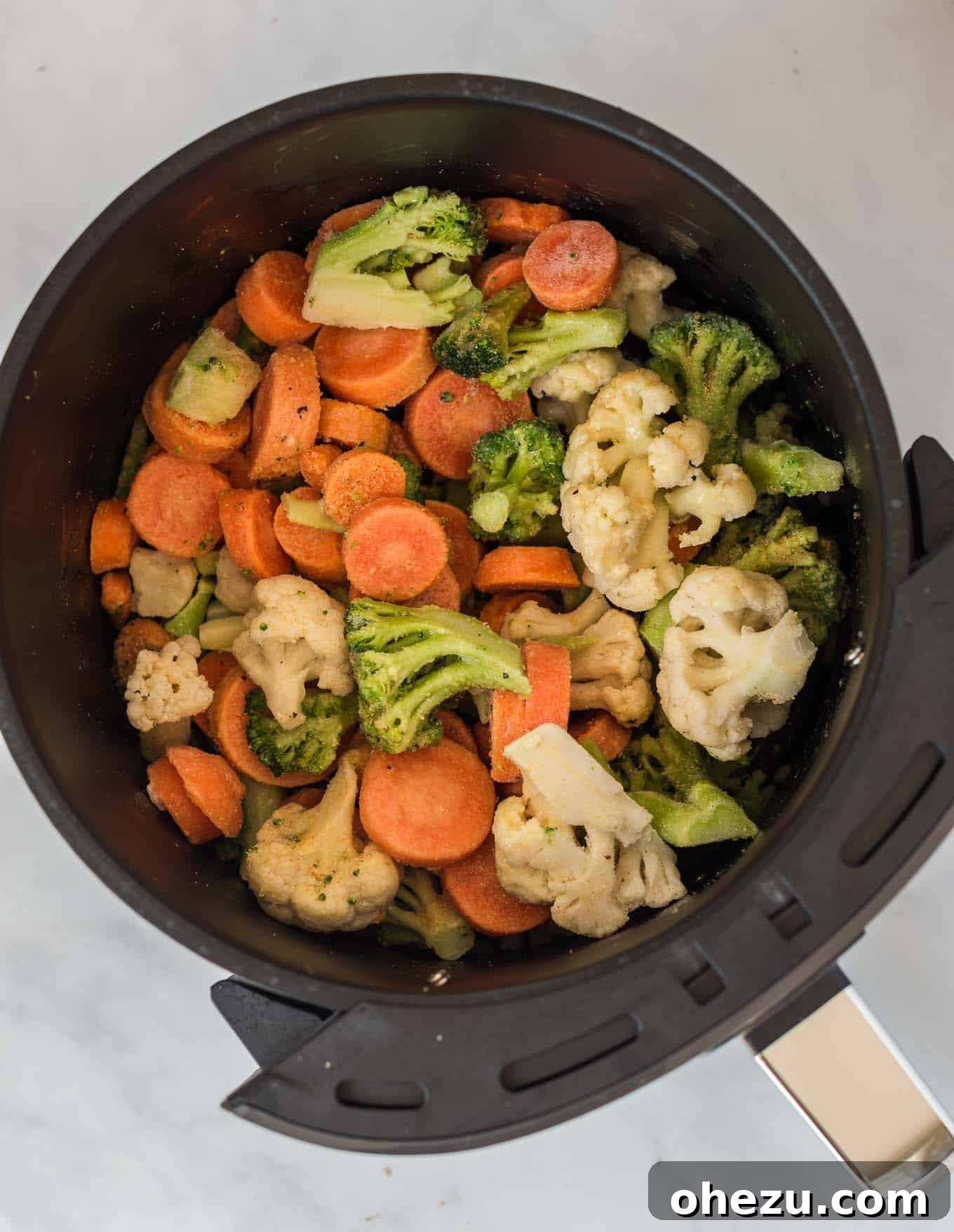 Frozen mixed vegetables are spread evenly in an air fryer basket, ready for cooking