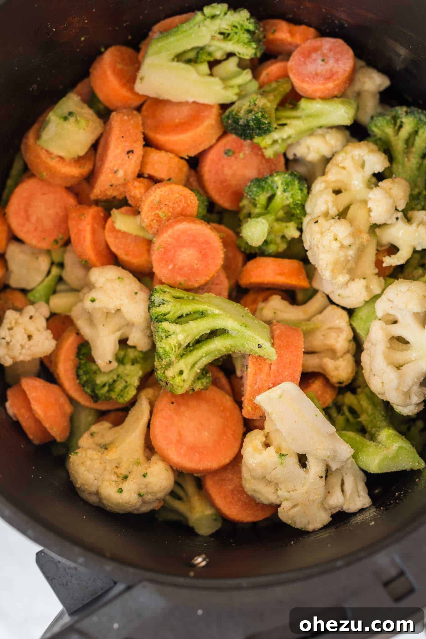 A close-up of frozen mixed vegetables spread out in an air fryer basket, showing texture before cooking