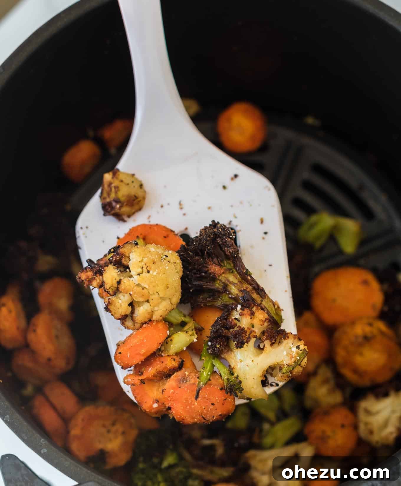 A white spatula scoops out a serving of perfectly air fried, crispy frozen vegetables from the basket