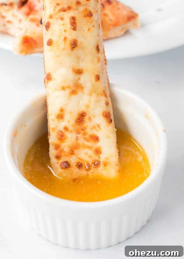 Delicious cheese stick being dipped into a rich, golden Papa John's style garlic sauce in a white ramekin.