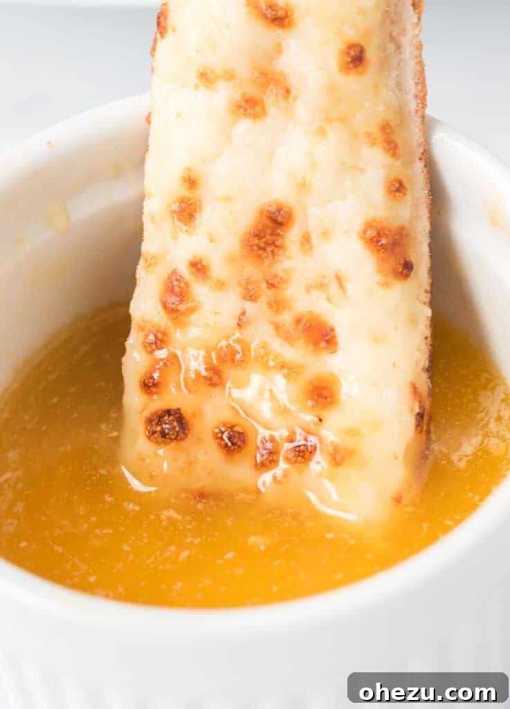 Crispy cheese sticks being dipped into a small white bowl of golden garlic sauce, highlighting its perfect dipping consistency.