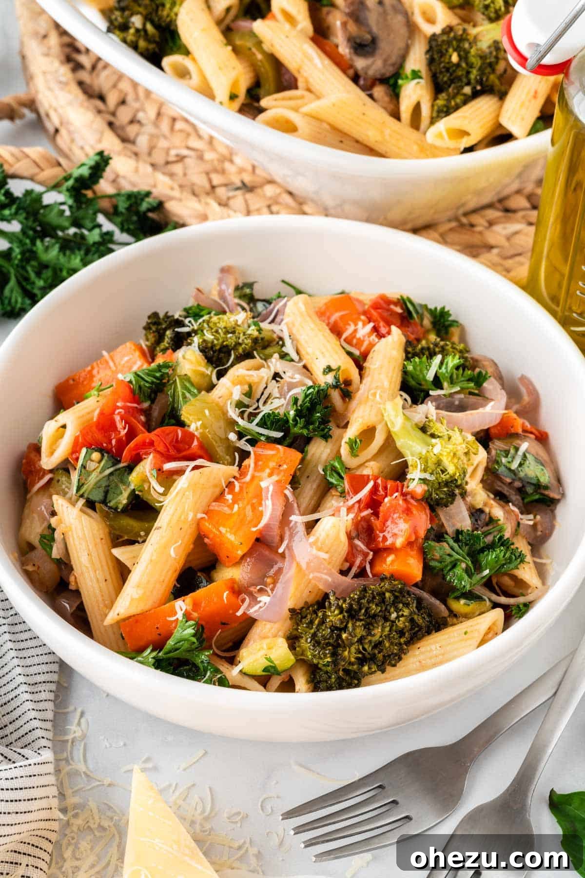 A white bowl of roasted vegetable pasta, generously topped with freshly grated Parmesan cheese, ready to be enjoyed.