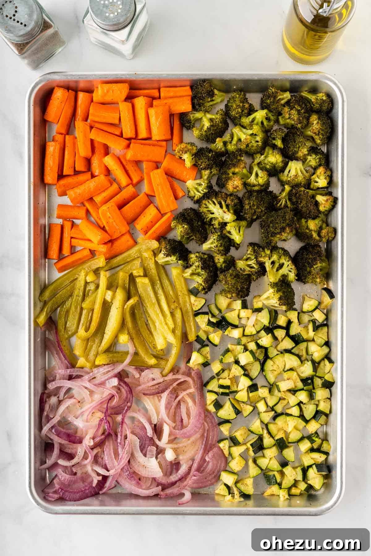 The first batch of vegetables – carrots, broccoli, bell peppers, onion, and zucchini – partially roasted on a baking sheet, showing light caramelization.