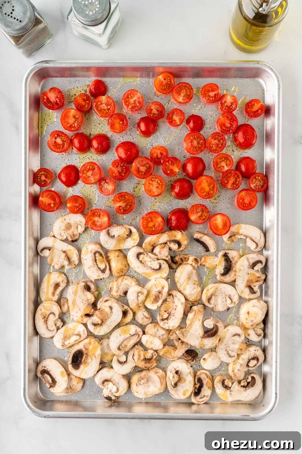 Sliced mushrooms and halved cherry tomatoes arranged on a baking sheet, seasoned and ready for roasting.