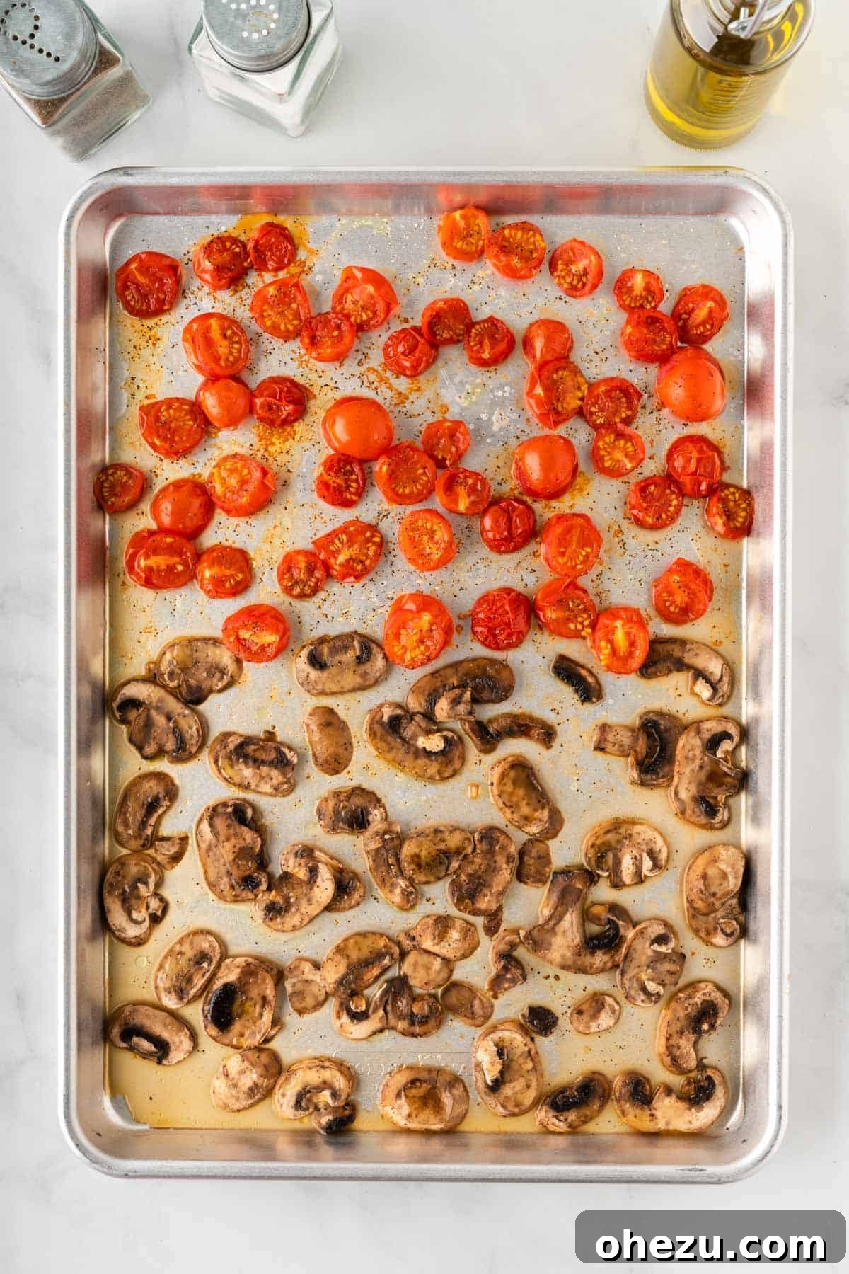 Roasted mushrooms and tomatoes on a baking sheet, showing their softened texture and enhanced color after being cooked.
