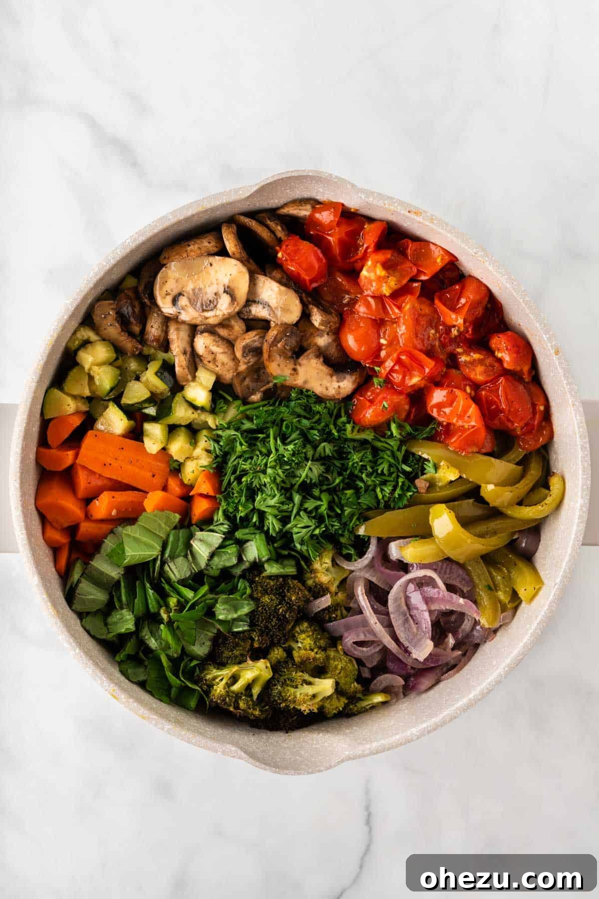 Hands adding the colorful roasted vegetables and fresh herbs into a pot of cooked pasta, ready for mixing.