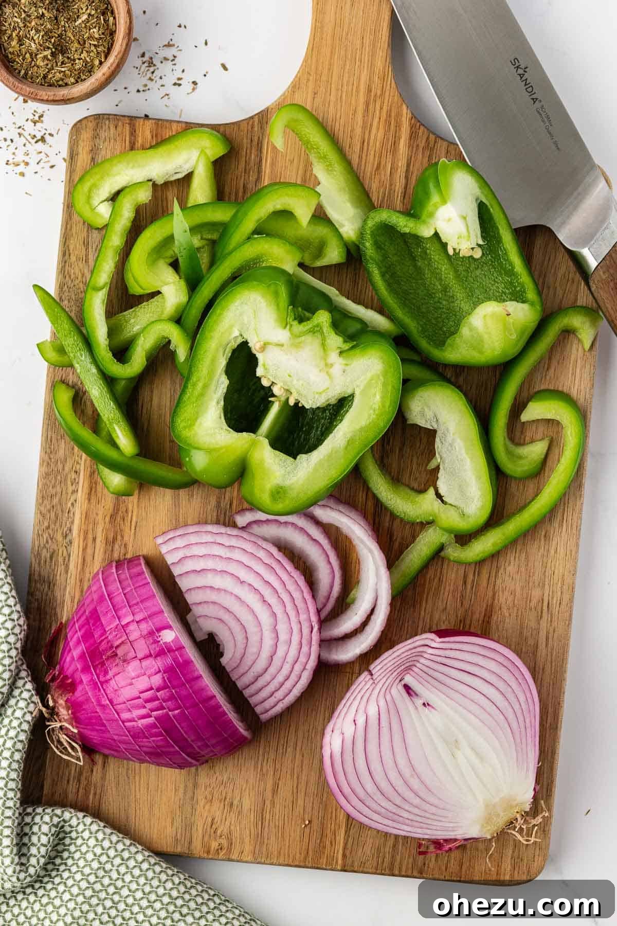 Zesty Fajita Medley 5 Uniformly sliced green bell pepper and red onion on a wooden cutting board, ready for cooking.
