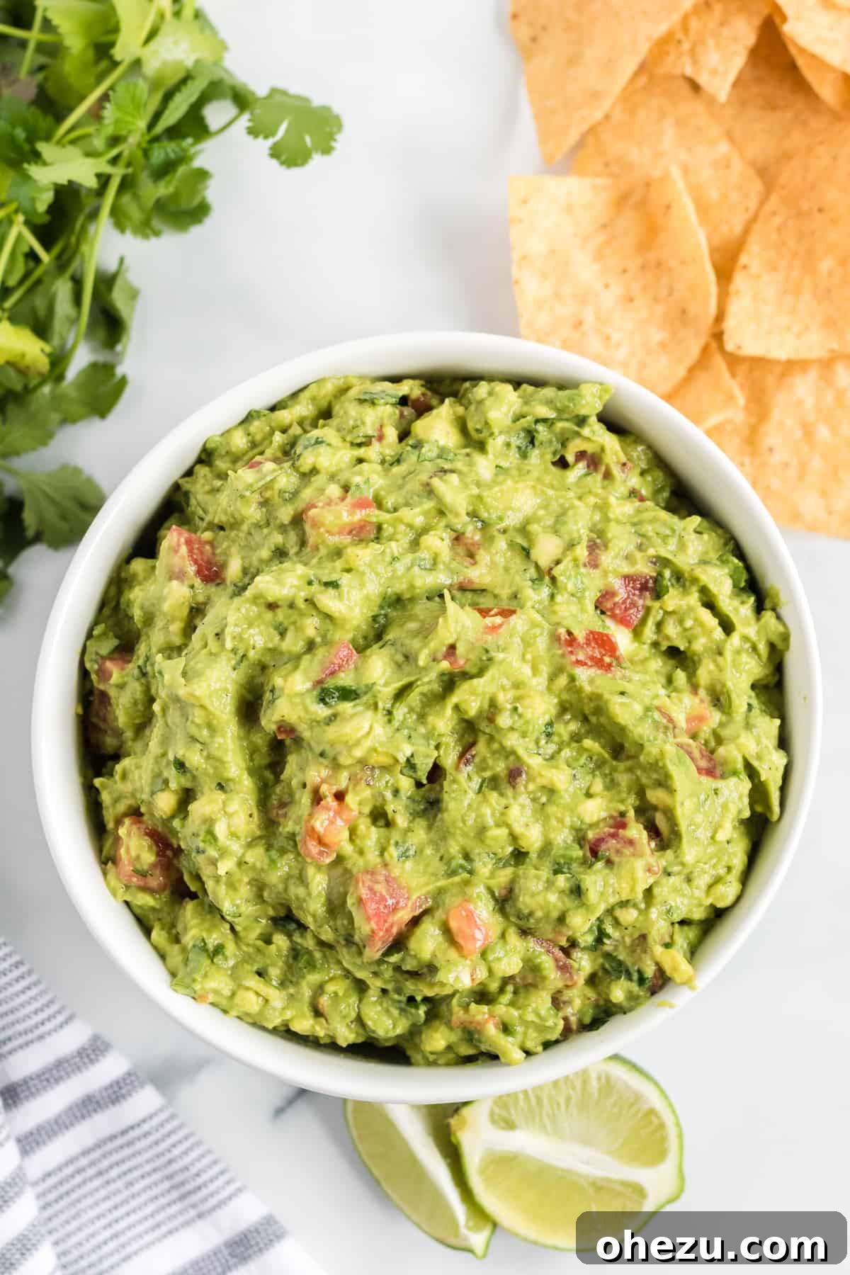 A close-up of fresh guacamole garnished with chopped tomatoes in a white bowl.