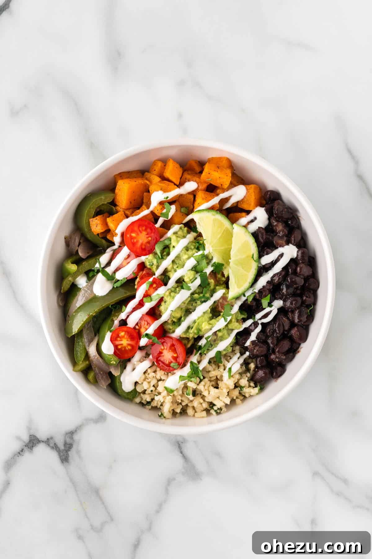 Drizzling sour cream over a completed cauliflower rice burrito bowl.