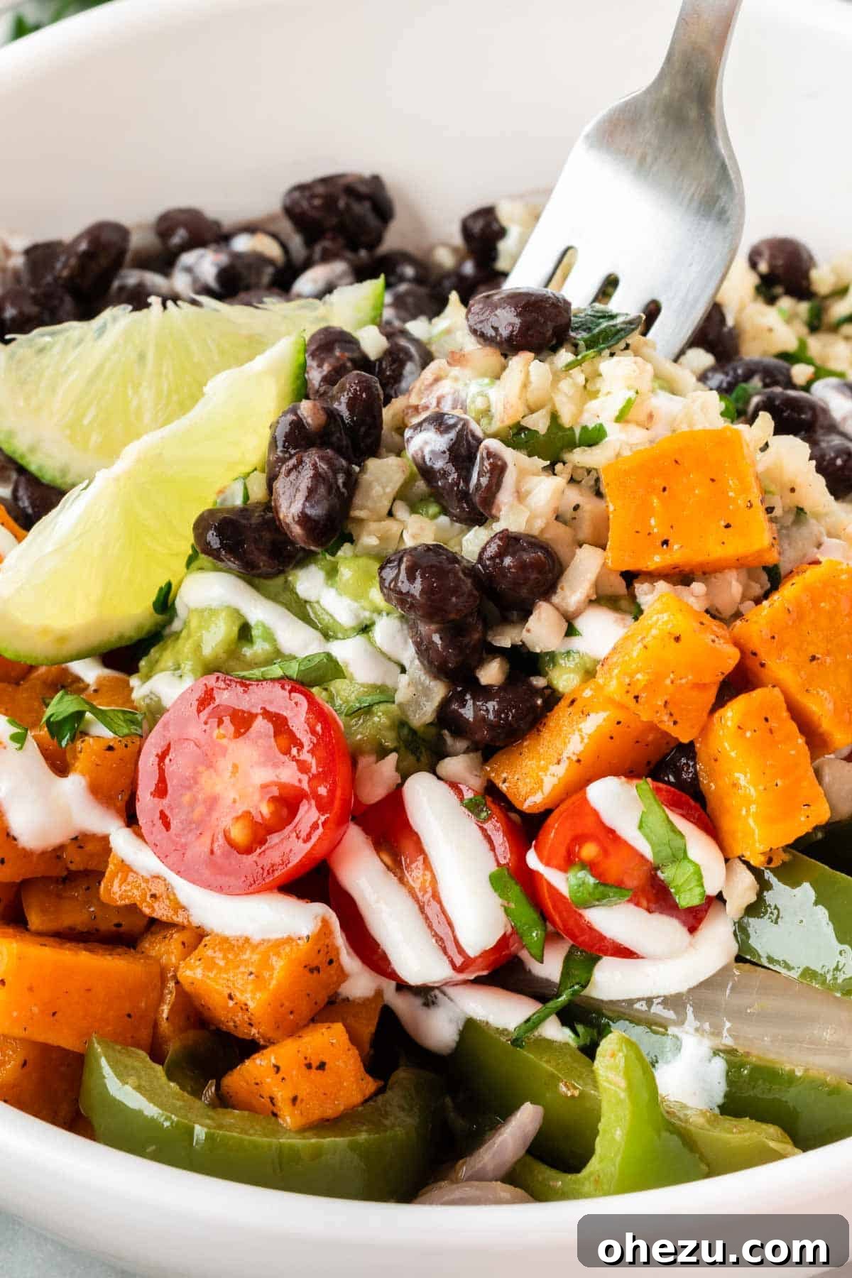 A beautifully assembled cauliflower rice burrito bowl with black beans, fajita veggies, sweet potatoes, and guacamole.