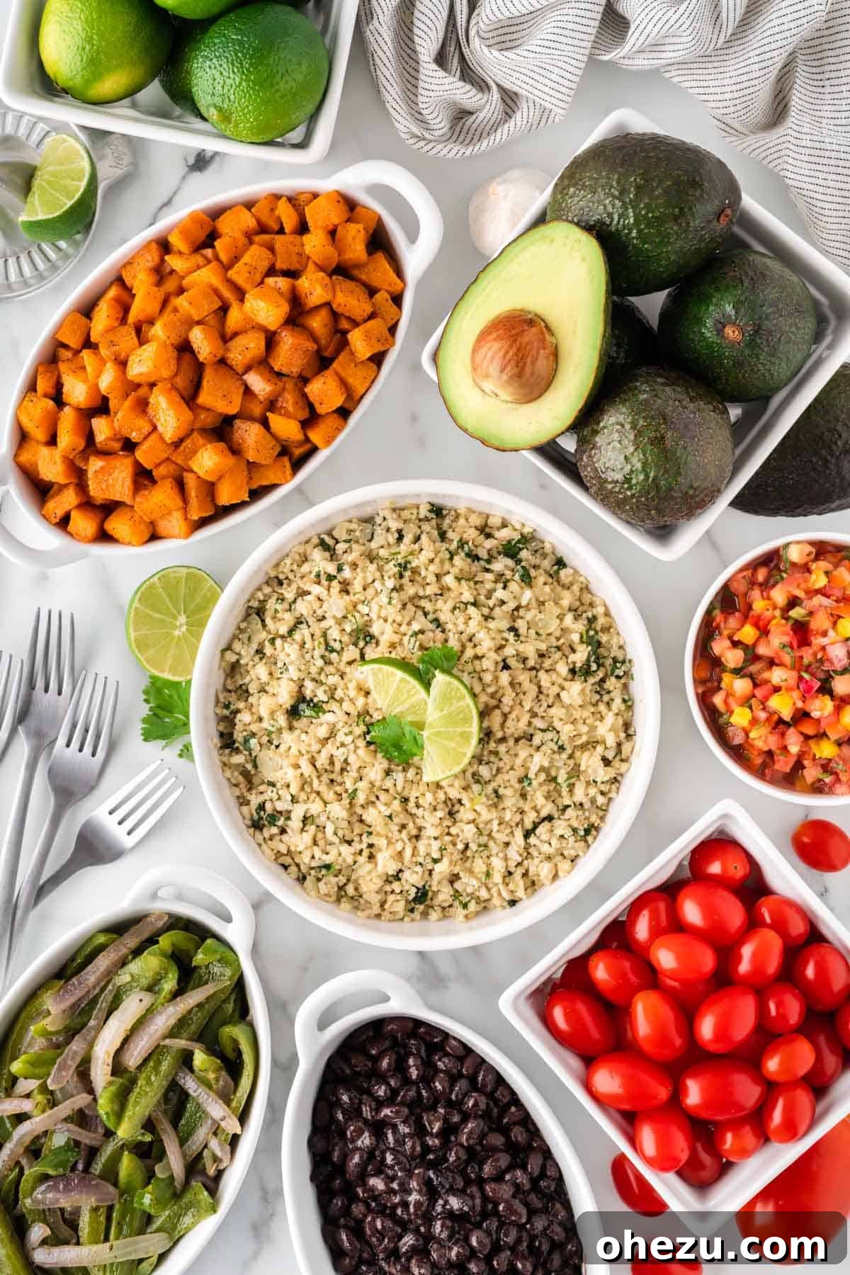 Various components for the cauliflower rice burrito bowl laid out in separate serving bowls, including roasted sweet potatoes, black beans, fajita veggies, and guacamole.