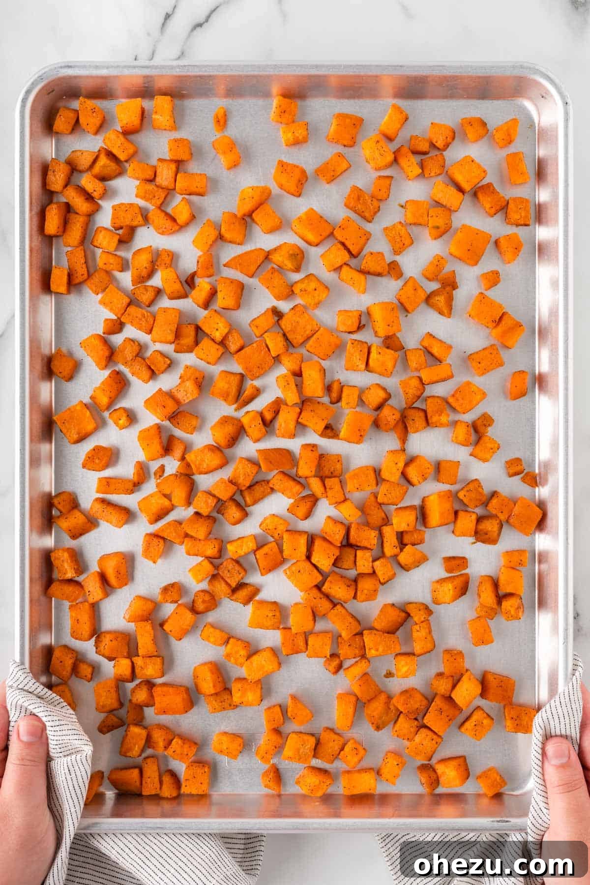 Cubed sweet potatoes spread on a baking sheet, ready for roasting.