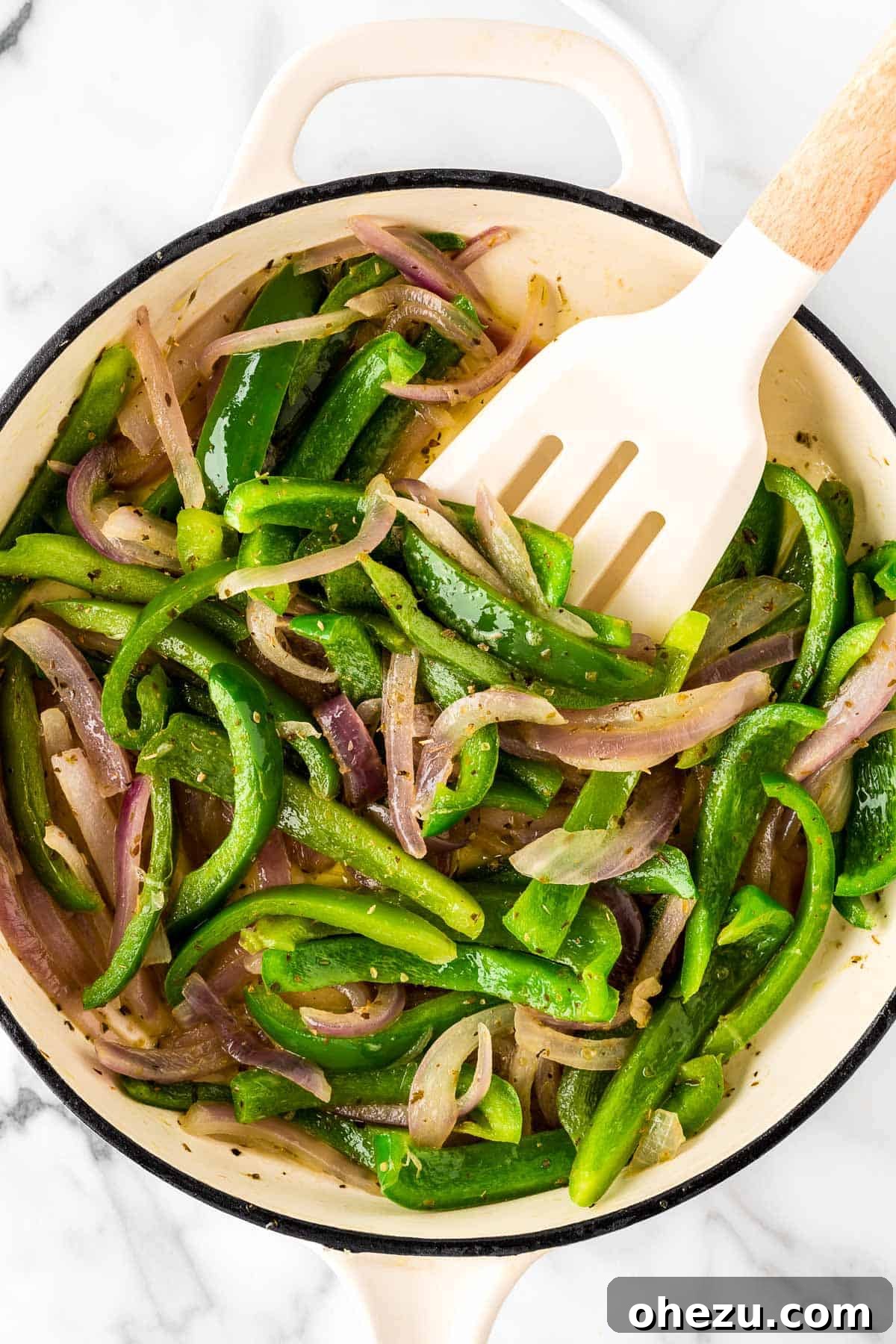 A hand stirring colorful fajita vegetables in a large skillet on the stove.