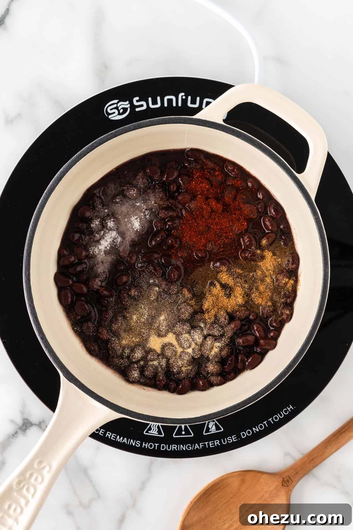 Adding various seasonings to black beans in a saucepan.