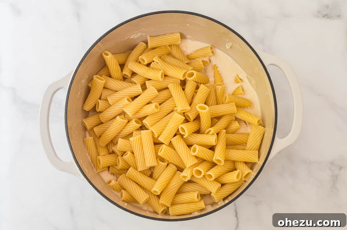 Creamy Spinach Artichoke Pasta Casserole 4 Cooked rigatoni pasta resting in a white Dutch oven, ready for the sauce and other ingredients