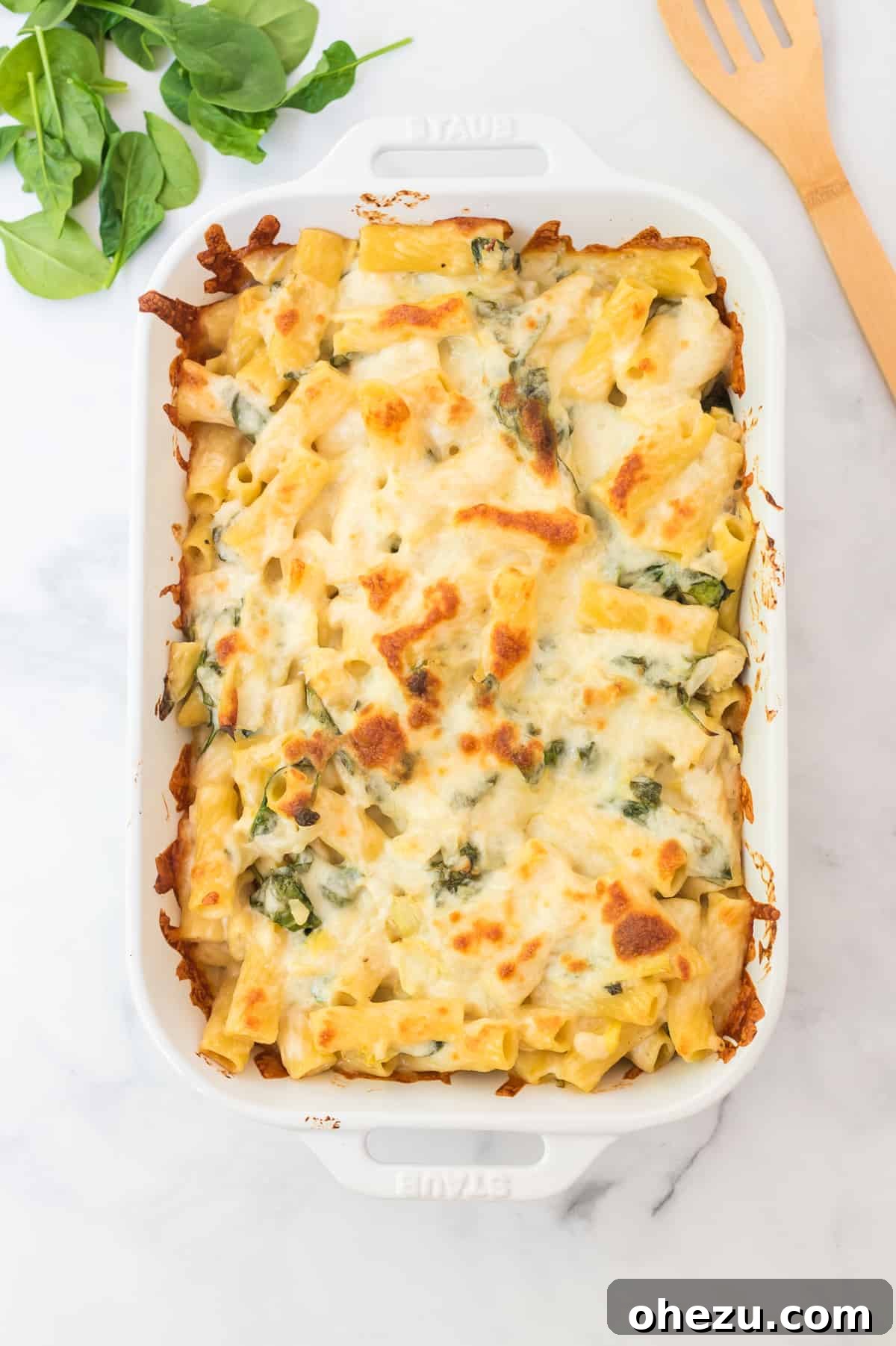 Creamy Spinach Artichoke Pasta Casserole 6 Close-up of a bubbling spinach artichoke pasta bake in a white baking dish, fresh out of the oven