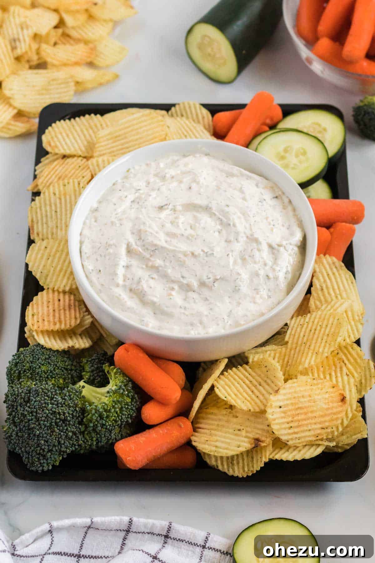 A vibrant platter featuring a bowl of chip dip surrounded by a diverse selection of fresh vegetables and chips, showcasing a healthy and inviting snack option.