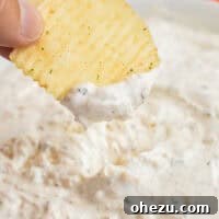 A ruffle chip being dipped into creamy sour cream dip, indicating the perfect appetizer.