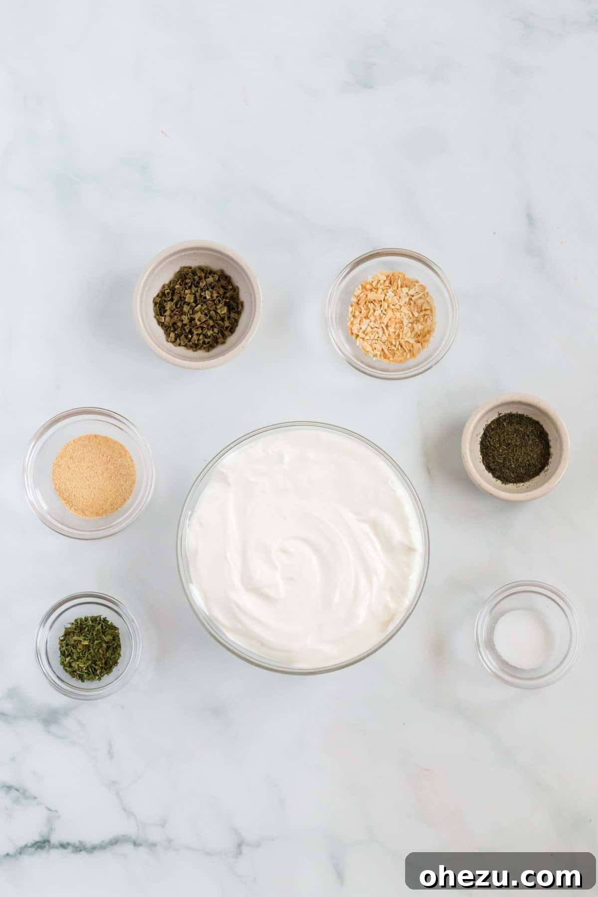 A flat lay of all the essential ingredients laid out on a clean surface, including sour cream, garlic powder, minced onion, dill, chives, parsley, and salt, ready to be combined.
