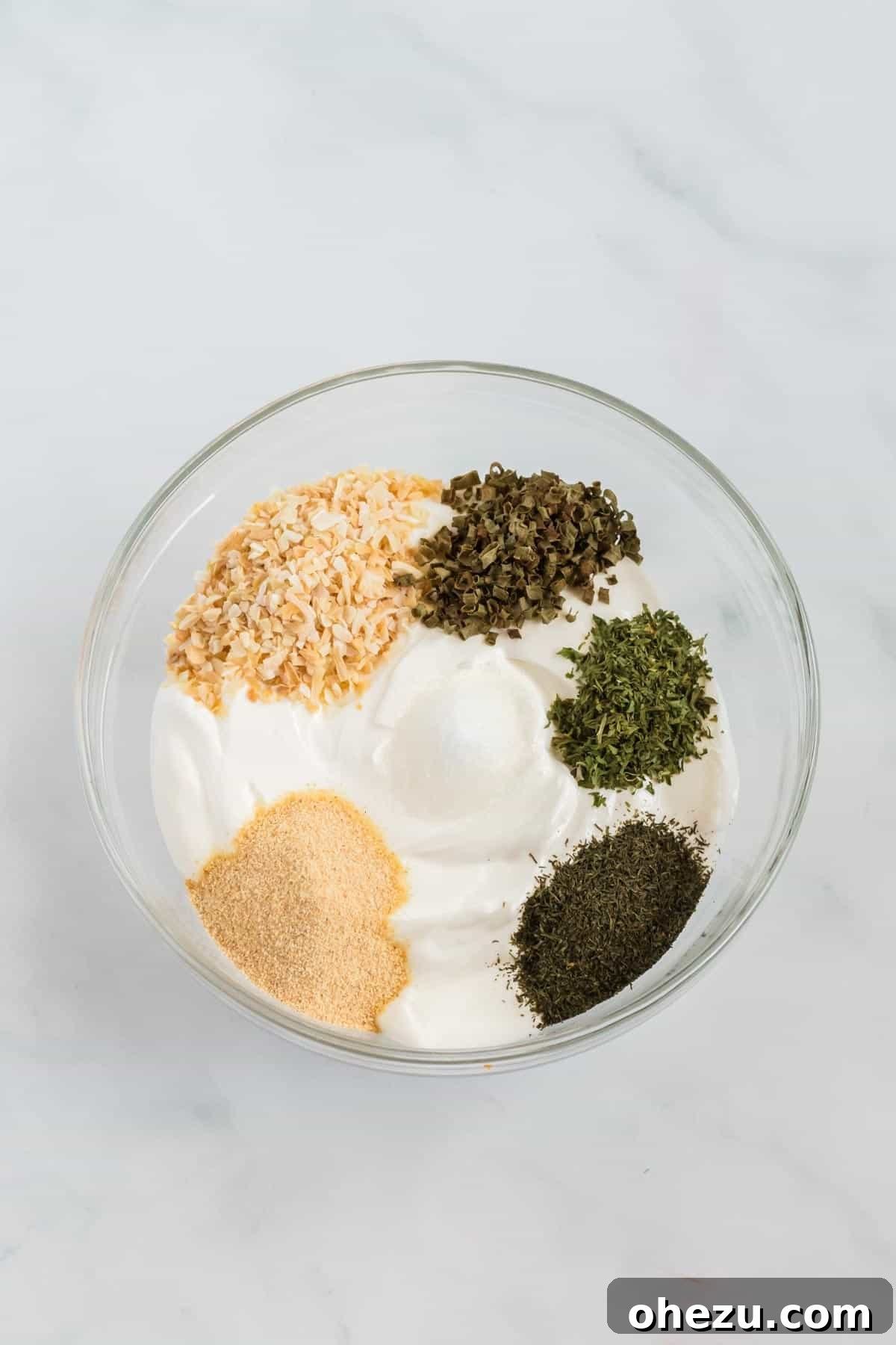 All the dry spices have been added to the creamy sour cream in a mixing bowl, showing the initial stage of combining ingredients.