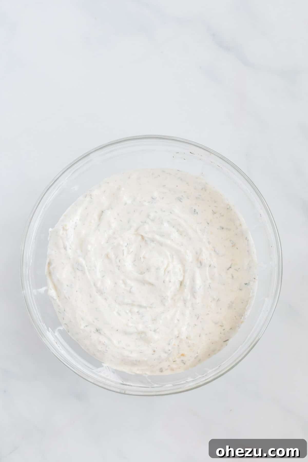 The sour cream dip has been thoroughly mixed and now sits in a bowl, showcasing its creamy texture and the flecks of herbs evenly distributed.