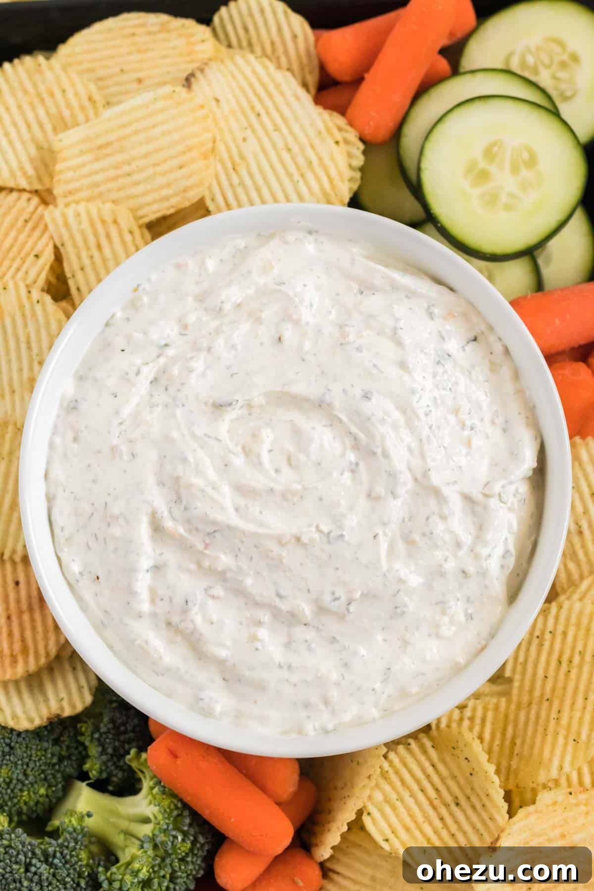 Another view of the chip dip in a bowl, surrounded by a variety of chips and fresh vegetables like broccoli, carrots, and cucumber, perfect for a healthy and delicious snack.
