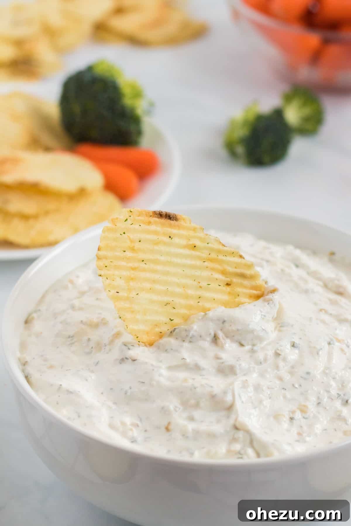 A close-up of a ruffle chip being generously dipped into the creamy homemade chip dip, highlighting the perfect scoop and appetizing texture.