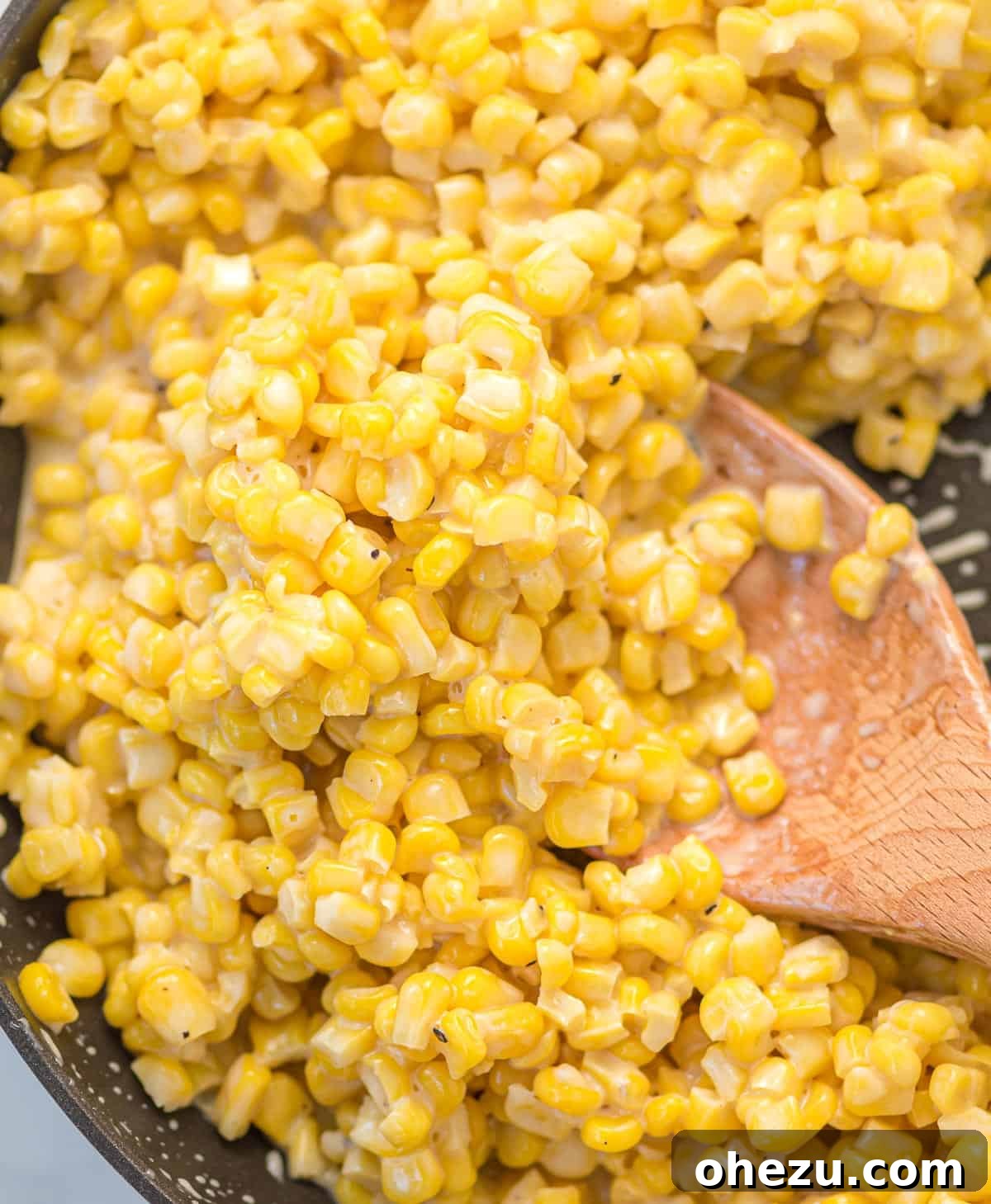 Honey butter corn being stirred in a skillet with a wooden spoon