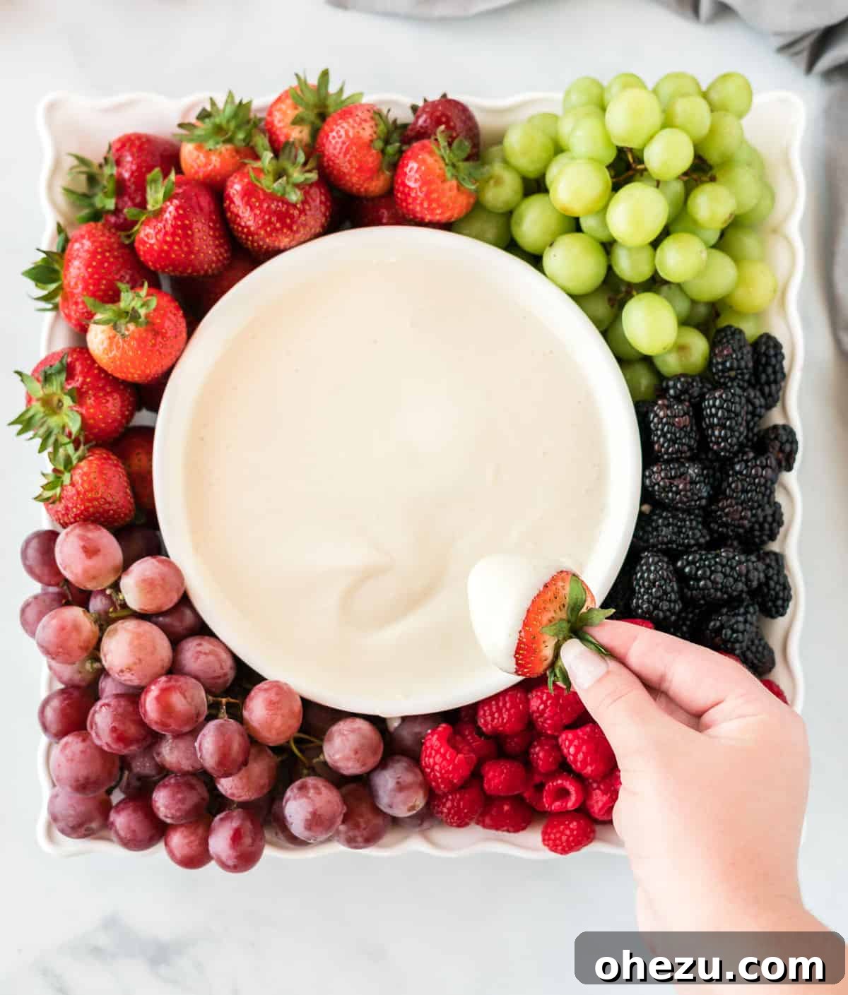 A vibrant tray laden with an assortment of fresh fruits, including berries and grapes, surrounding a bowl of creamy cream cheese yogurt dip.