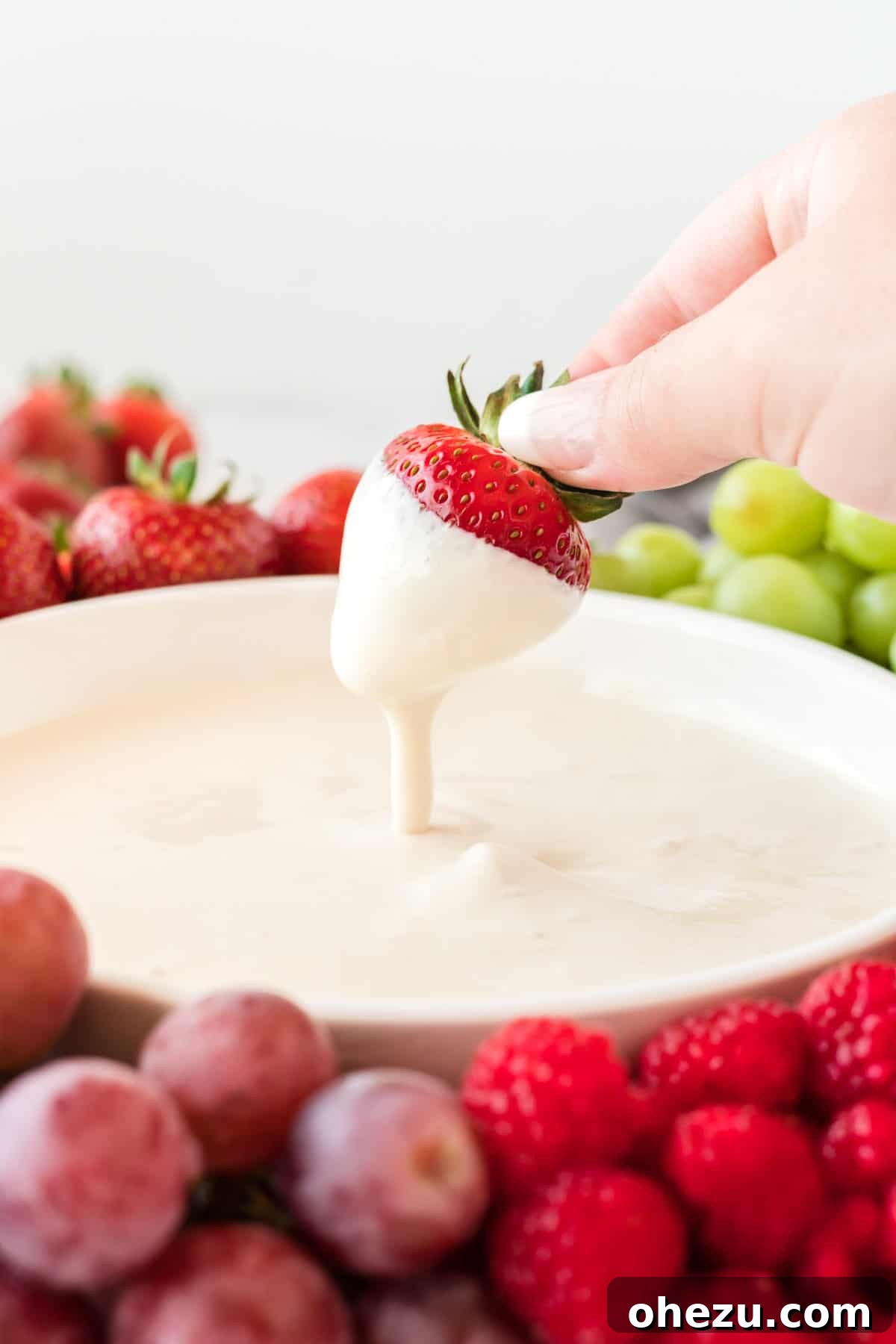 A single juicy strawberry being dipped into a bowl of the creamy cream cheese yogurt dip, highlighting its smooth texture.