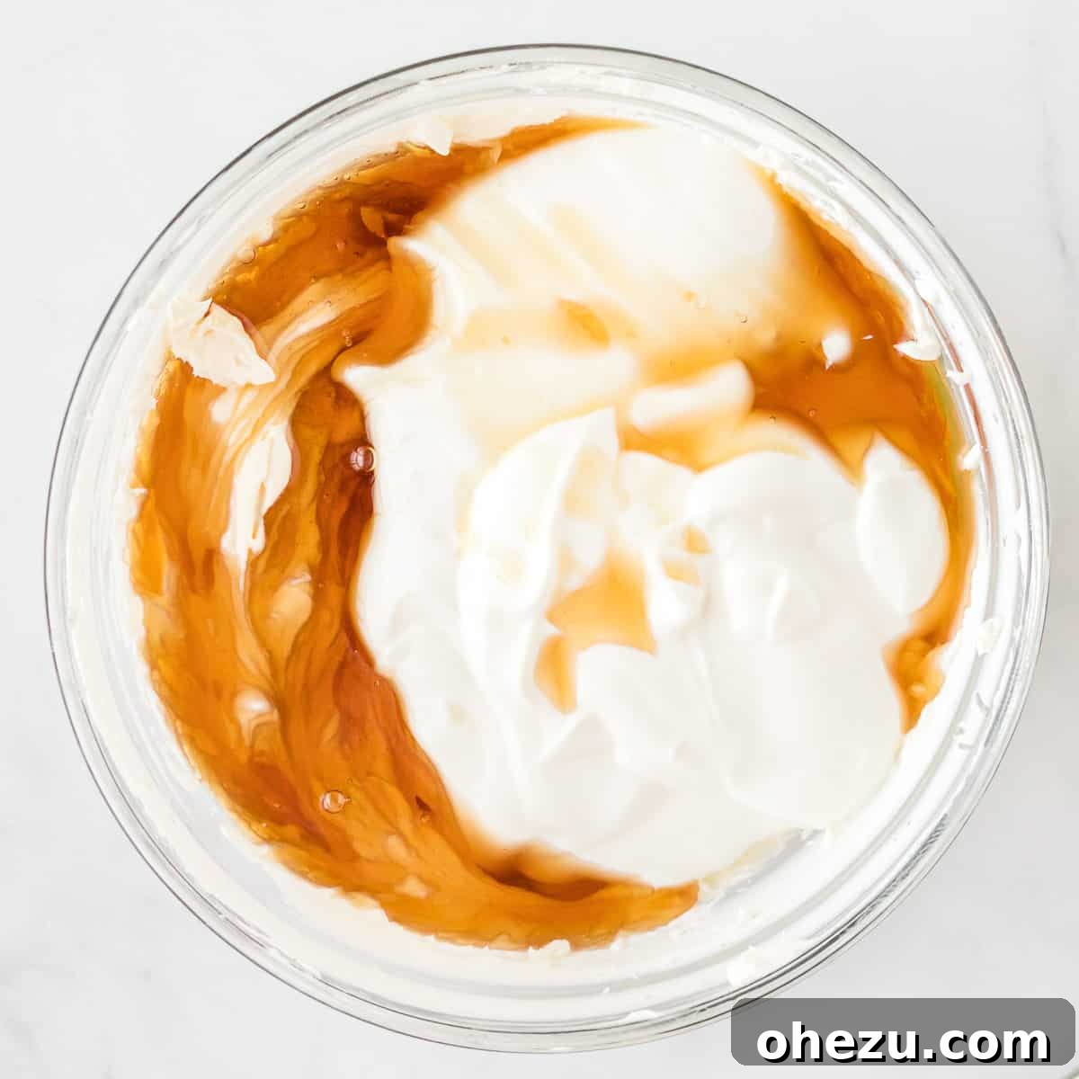 Pure maple syrup and plain Greek yogurt being added to the beaten cream cheese in a mixing bowl.