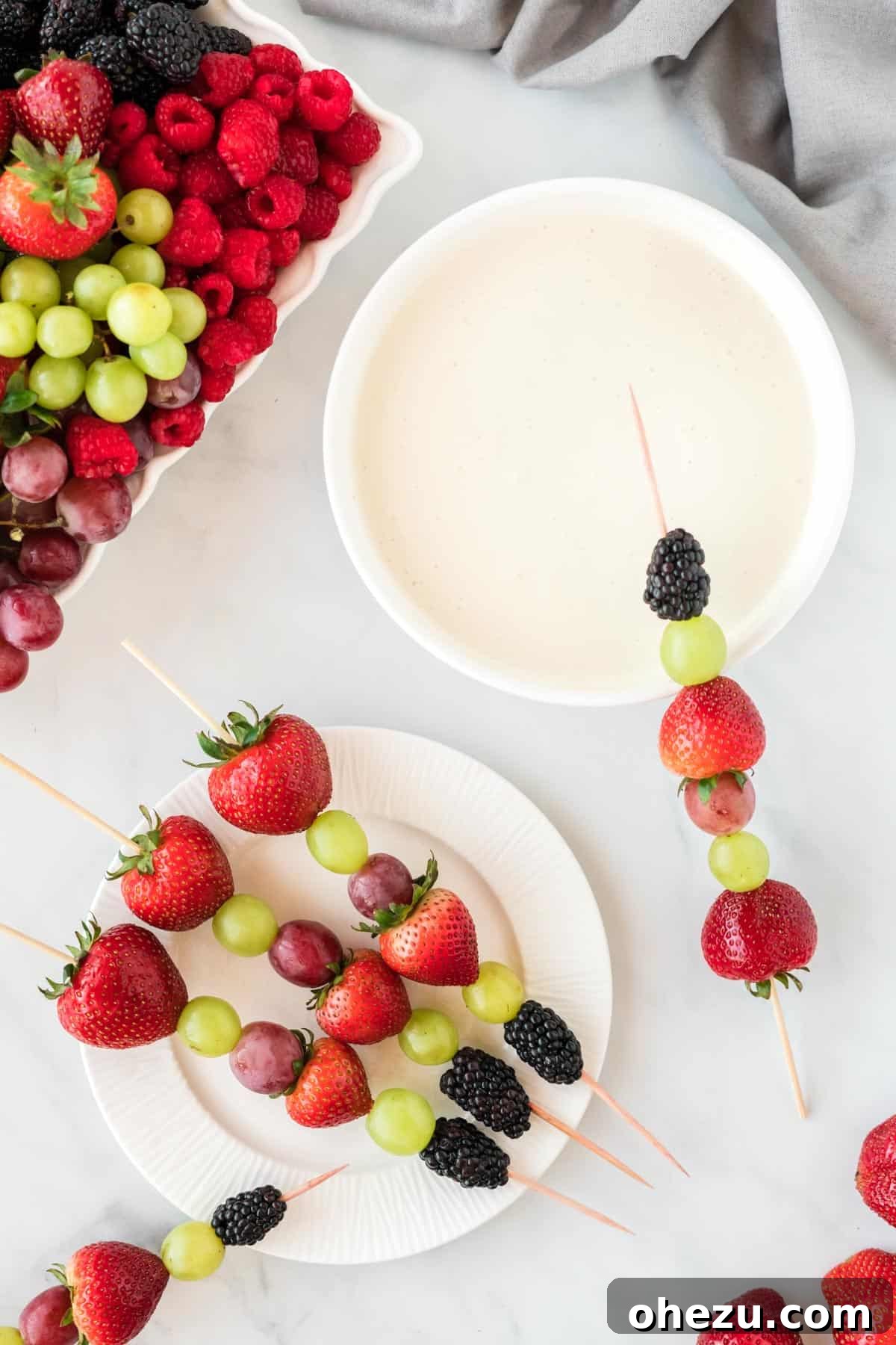 A beautiful arrangement of fruit skewers featuring strawberries, grapes, and blackberries, served alongside a bowl of creamy fruit dip.