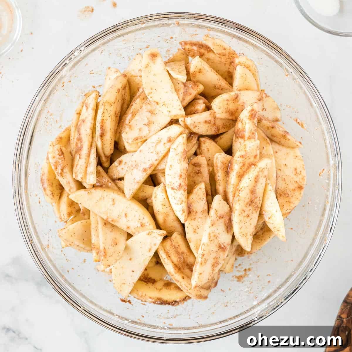 Sliced apples mixed with cinnamon, granulated sugar, lemon juice, and flour in a mixing bowl