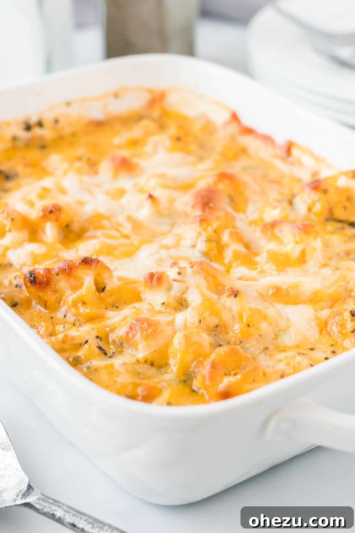 A bubbling white baking dish filled with golden-brown cheesy cauliflower casserole, ready to serve.