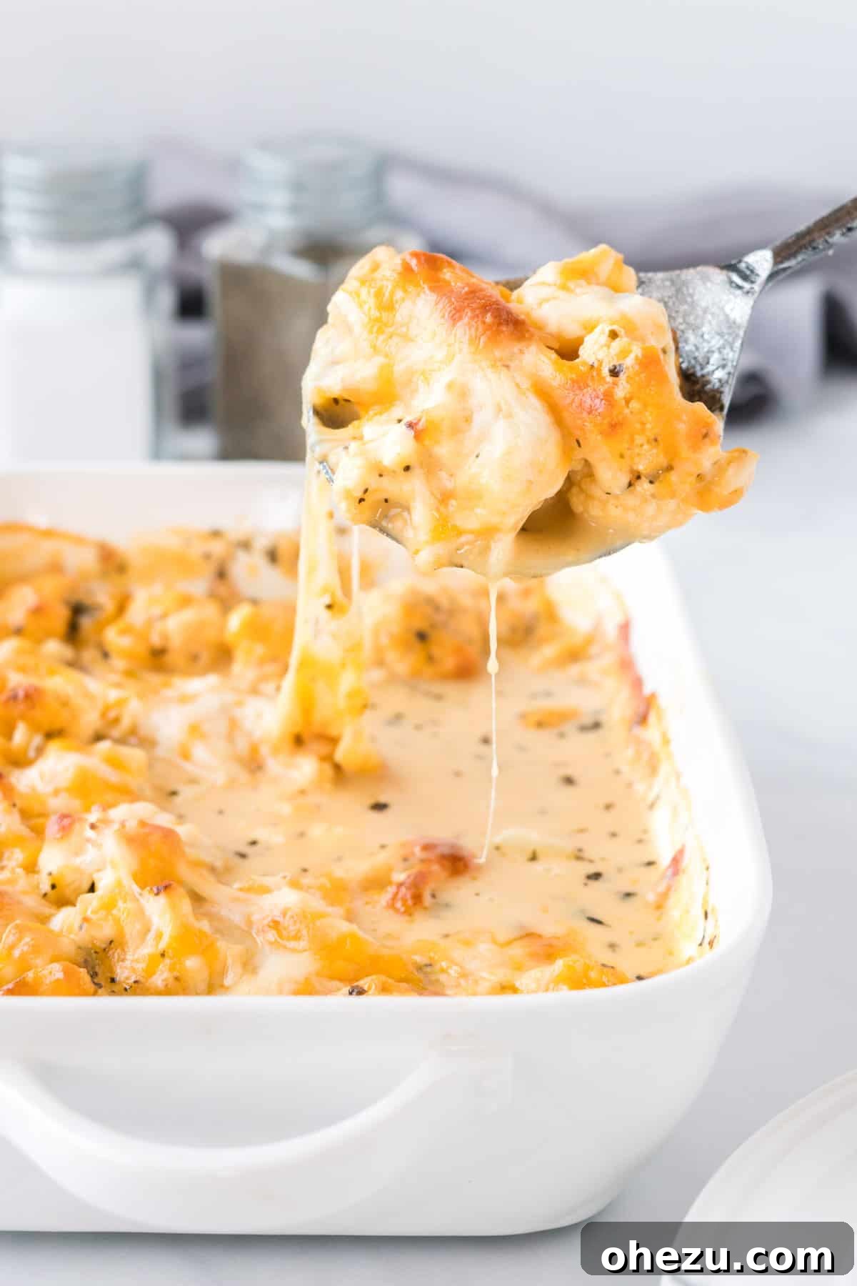 A spoon scooping a generous portion of cheesy cauliflower from the baking dish, showing its creamy texture.