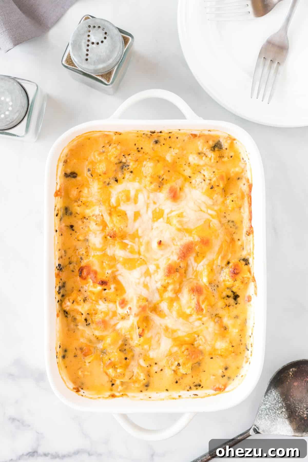 A beautifully baked cheesy cauliflower casserole, golden brown and bubbly, presented in a white baking dish.