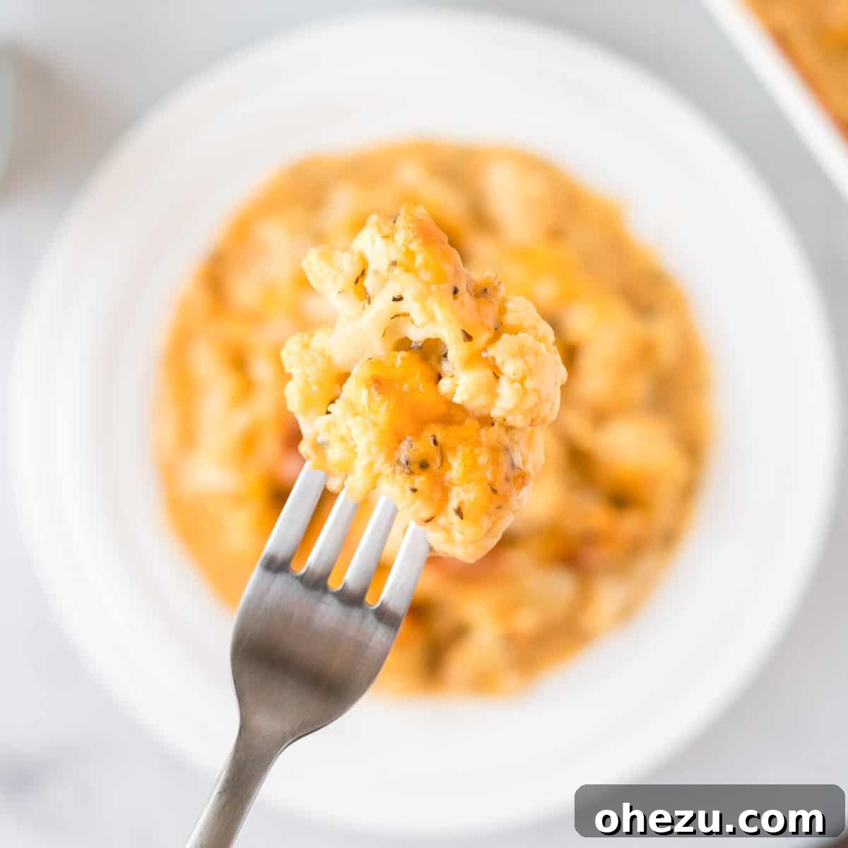 A fork holding a piece of cheesy cauliflower, showing the melted cheese and tender cauliflower texture.